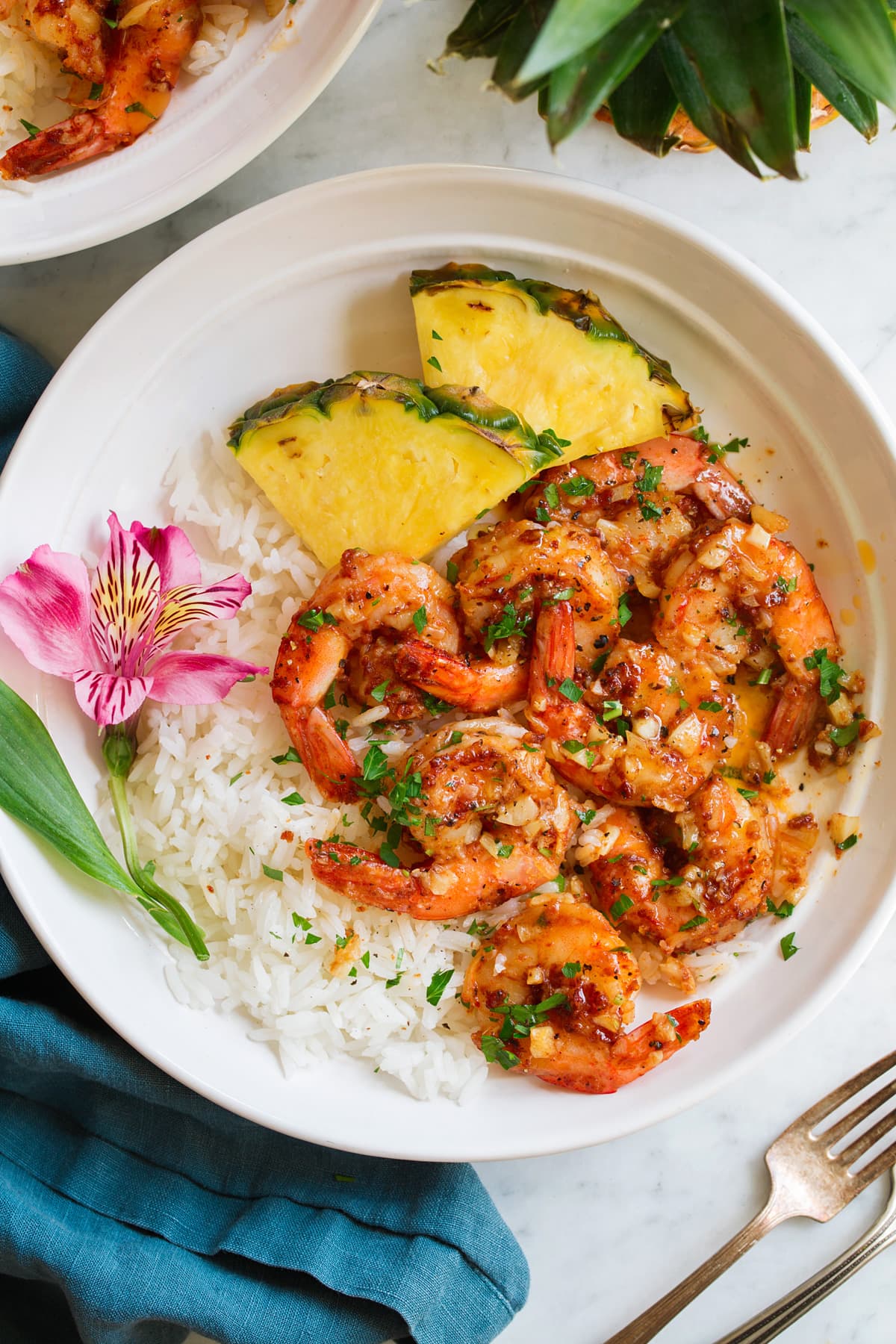 Gamberetti Hawaiani All'aglio Garlic shrimp in a shallow white bowl with rice, pineapple and a fresh tropical flower for decoration.