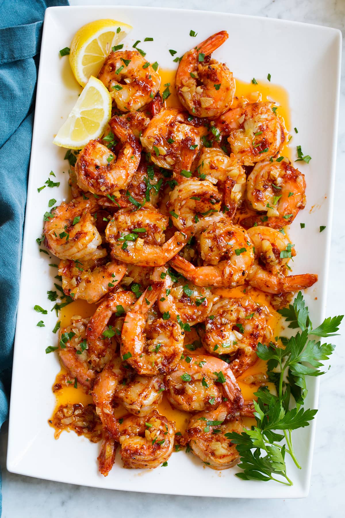 Gamberetti Hawaiani All'aglio Overhead image of Hawaiian garlic shrimp on a white platter. It is garnished with fresh lemon wedges and parsley.
