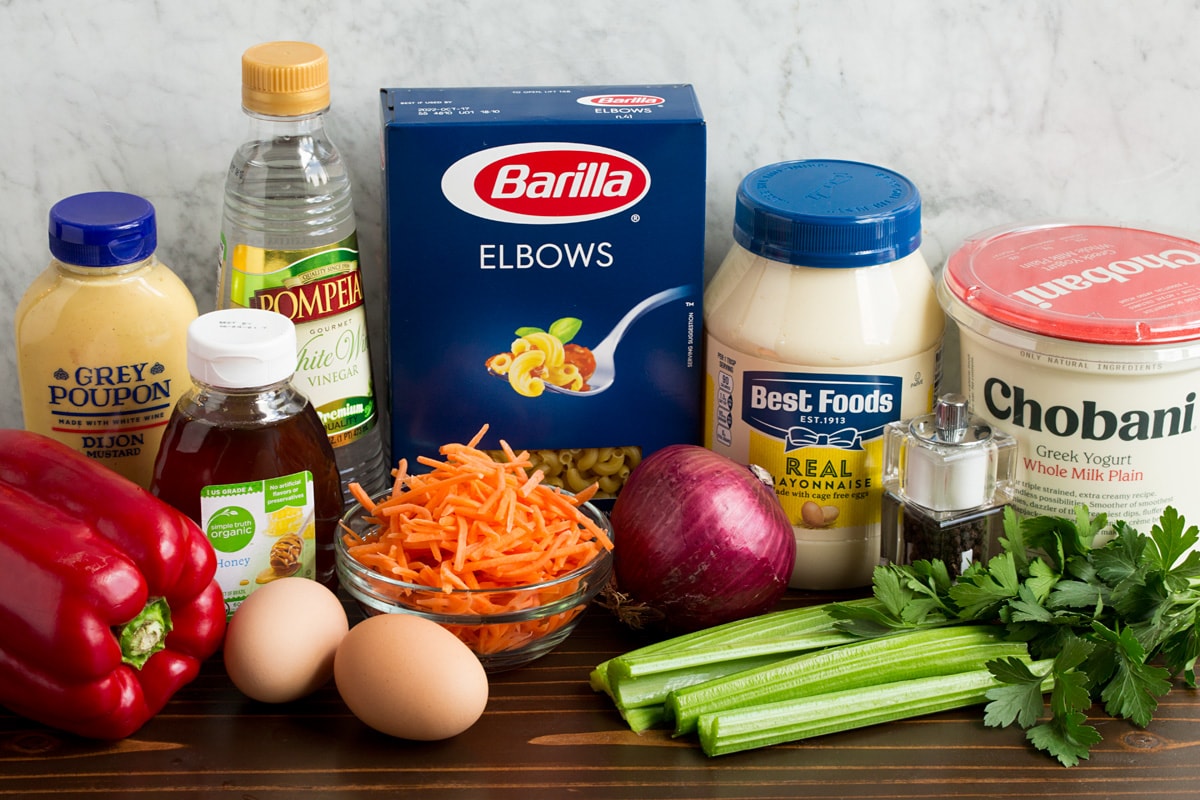Insalata di pasta Ingredients that are in macaroni salad shown here. Includes mayonnaise, Greek yogurt, dijon mustard, honey, eggs, carrots, bell pepper, celery, parsley, vinegar, salt and pepper.