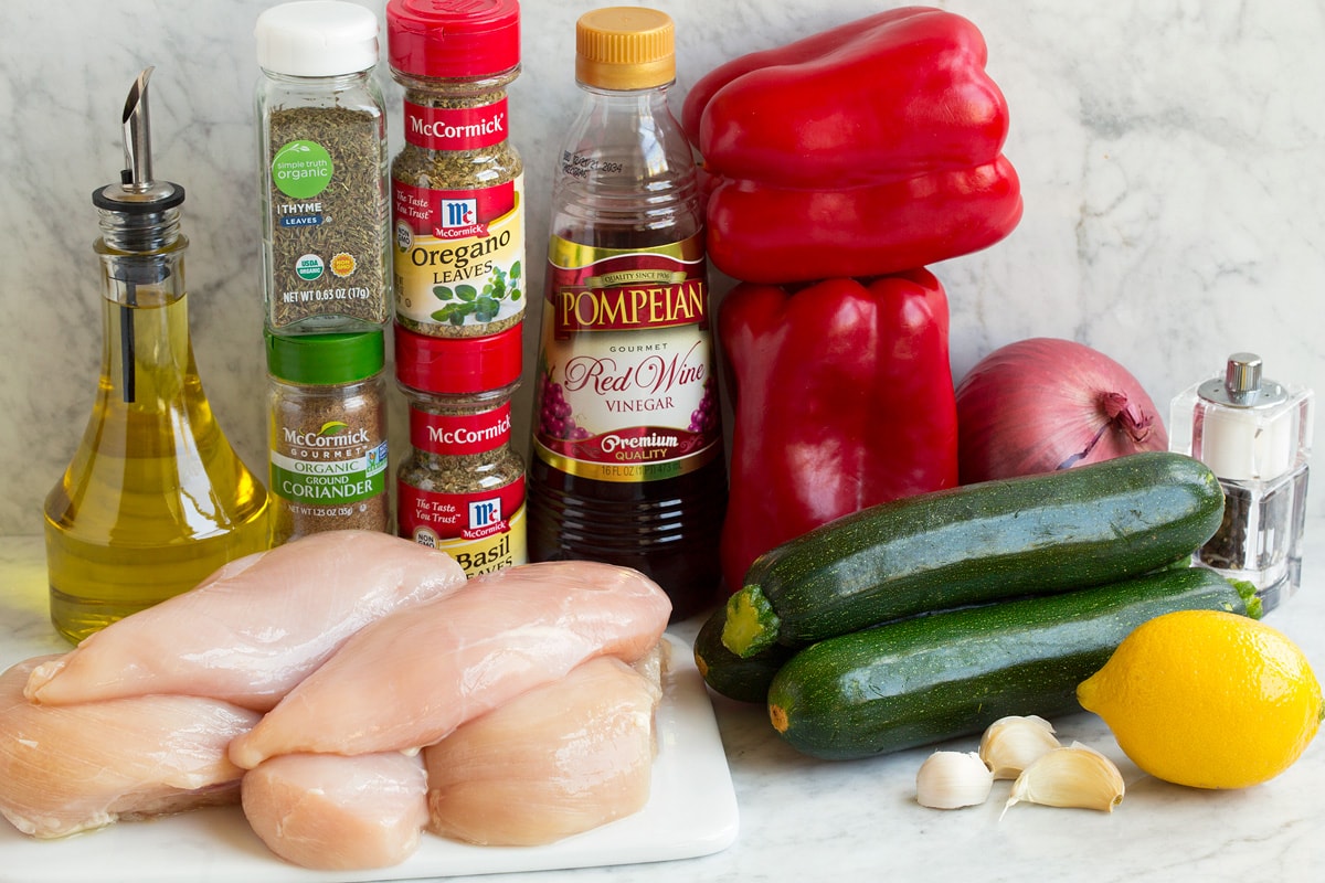 Collage di 6 immagini che mostrano i passaggi per preparare la marinata, ammollo del pollo greco, condire le verdure con olio, infilare gli ingredienti negli spiedini e grigliare i kebab. Ingredients that are used to make chicken kebabs shown in this image. Includes chicken breasts, herbs, vinegar, oil, lemon, and fresh vegeables.