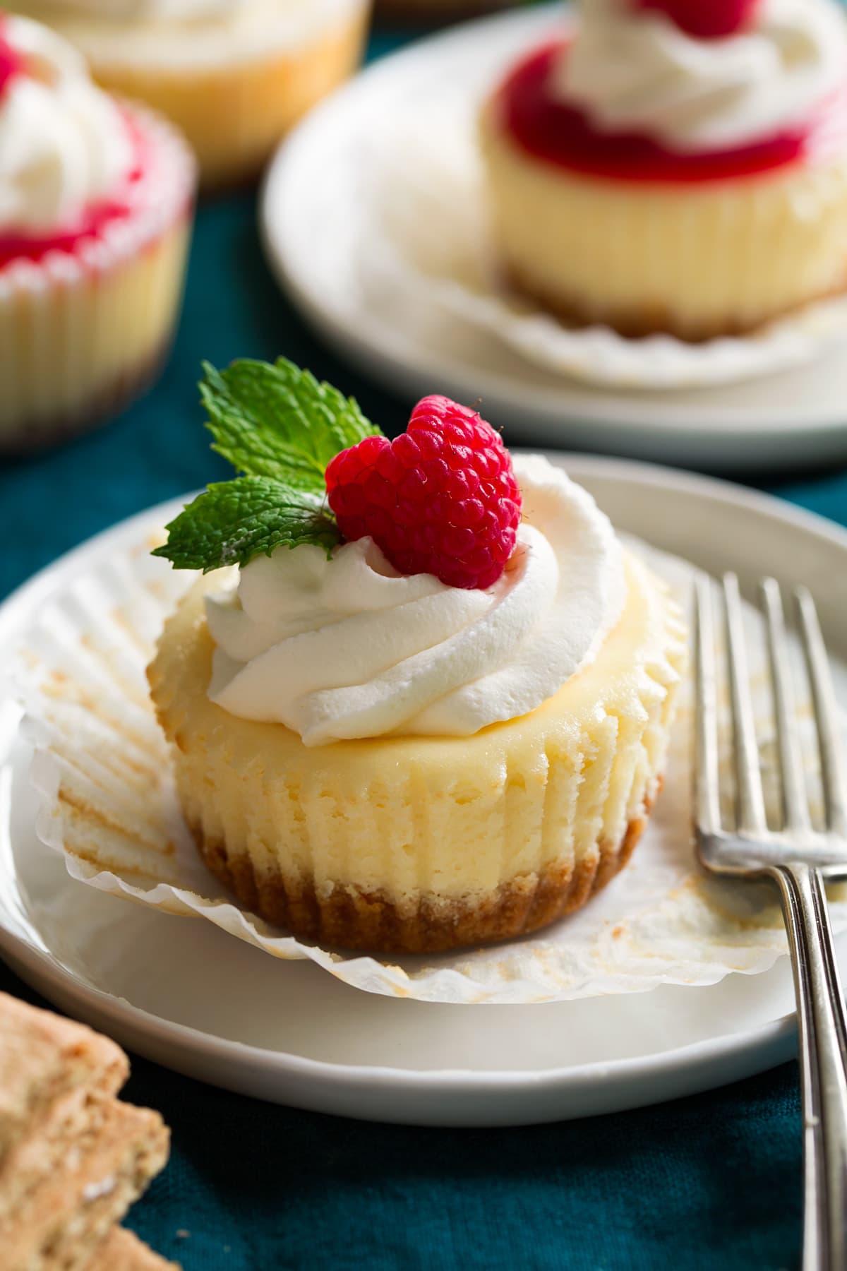 Mini cheesecakes Mini cheesecake shown on a dessert plate unwrapped from cupcake liner. It is topped with whipped cream, fresh raspberry and mint.