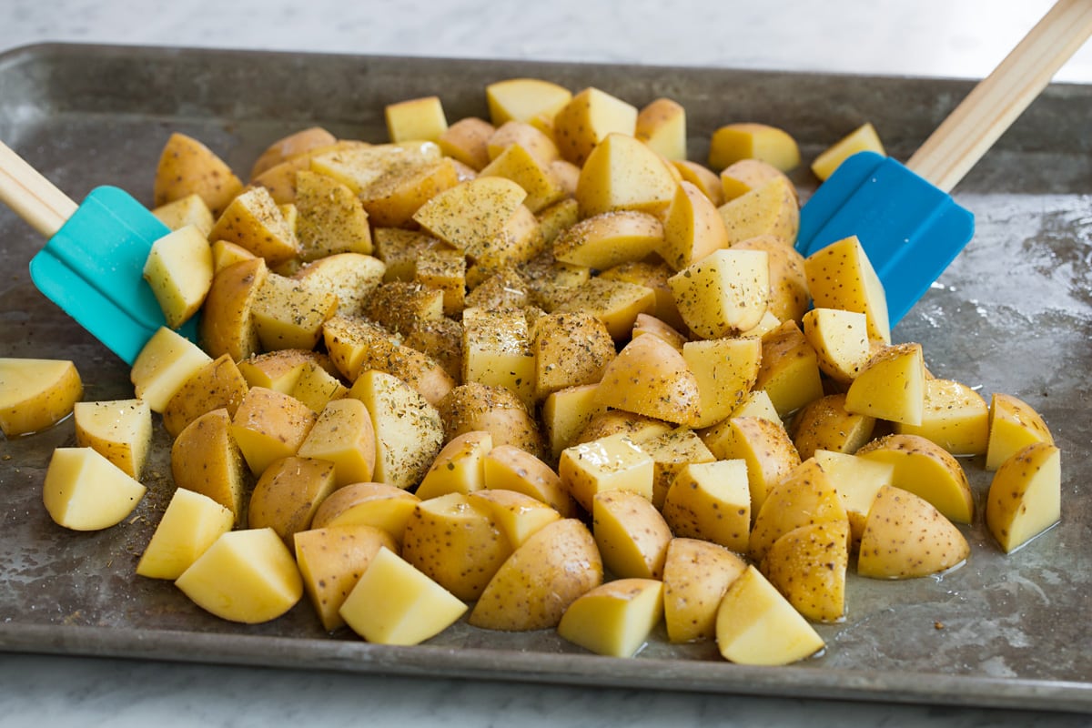 Patate Al Forno Al Limone Tossing potatoes with oil, lemon and seasonings using silicone spatulas. Potatoes are on a alluminum baking sheet.