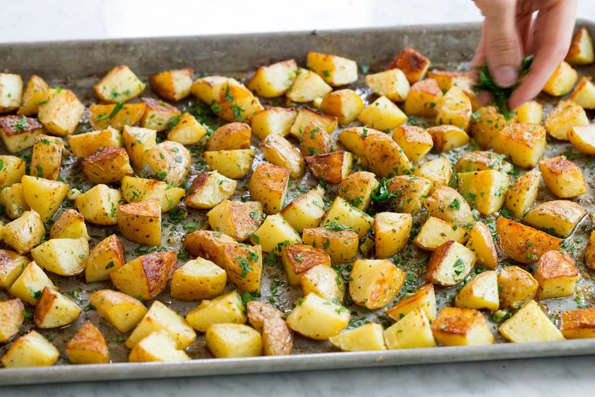 Patate Al Forno Al Limone Hand sprinkling roasted potatoes with parsley.