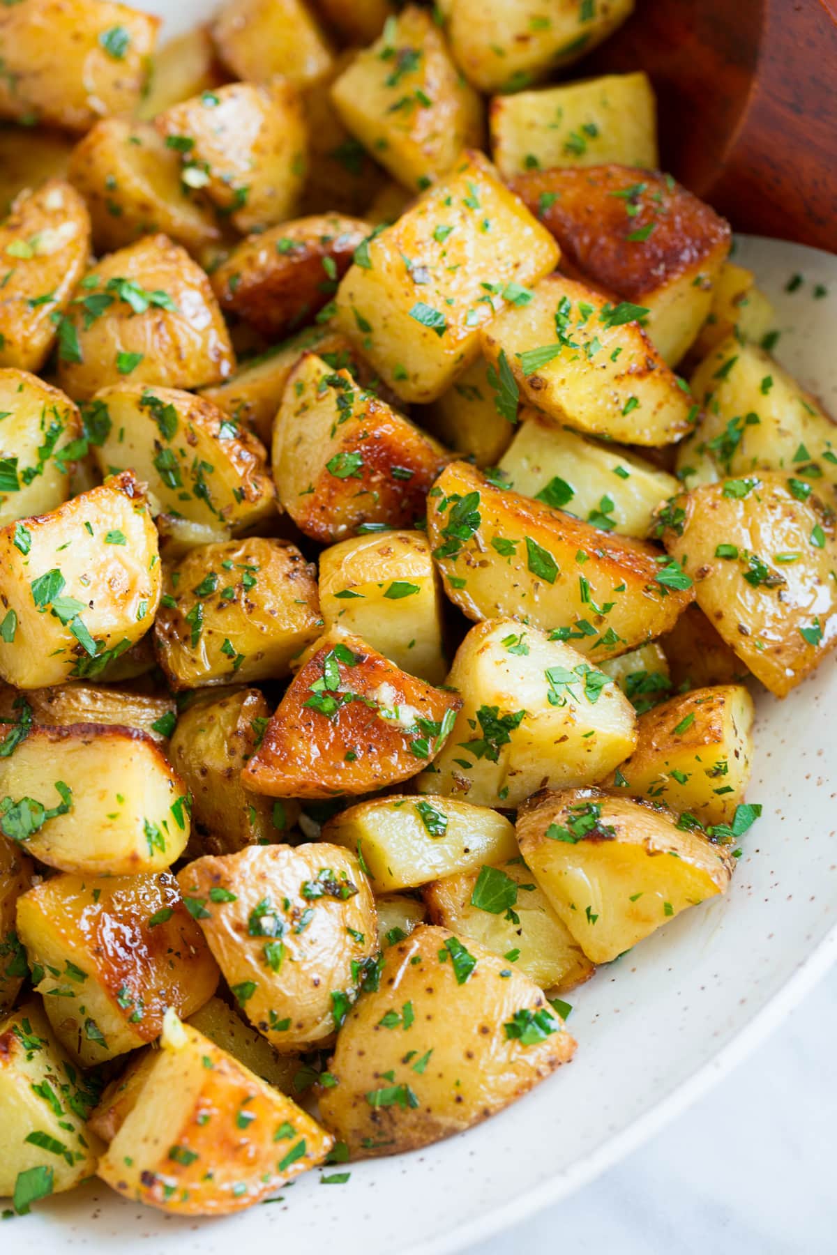Patate Al Forno Al Limone Close up image of roasted potatoes with lemon and parsley in a white serving bowl.