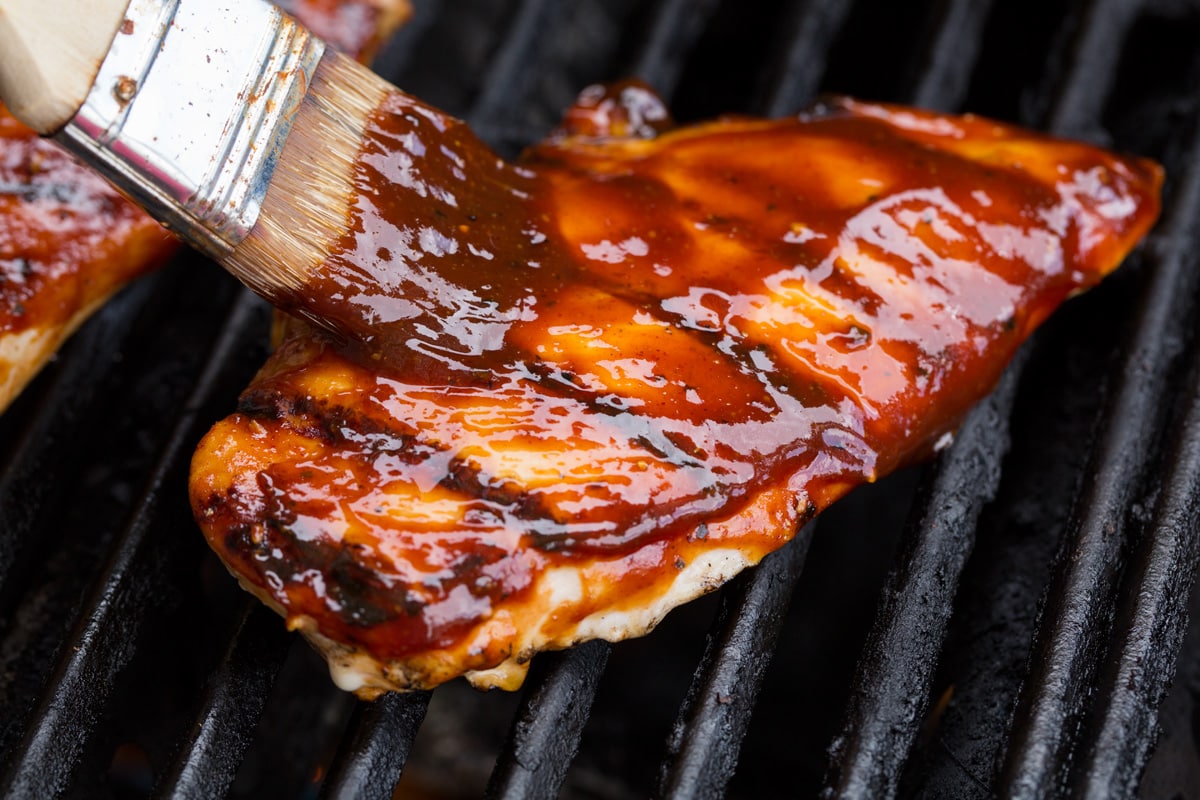 Salsa barbecue fatta in casa Basting chicken breast on grill with bbq sauce.