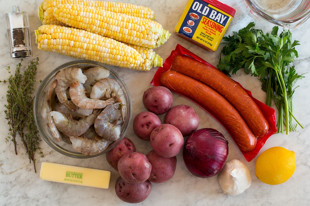 Bollire i gamberetti Image of ingredients used to make shrimp boil. Includes shrimp, corn on the cob, andouille sausage, red potatoes, onion, butter, lemon, parsley, thyme, garlic, salt and pepper and water.