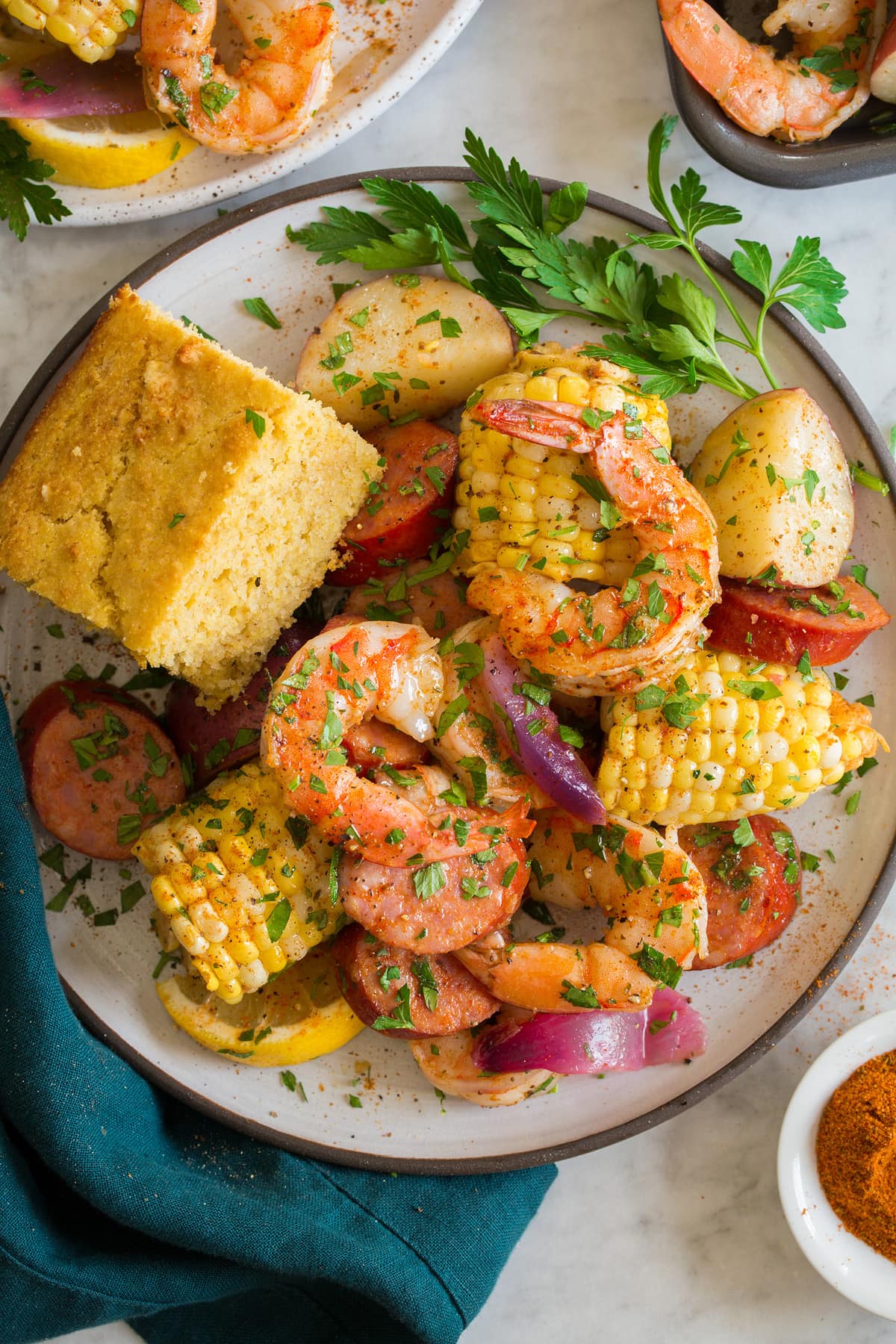 Bollire i gamberetti Image showing single serving of shrimp boil on a white plate with a serving suggestion of a side of cornbread.