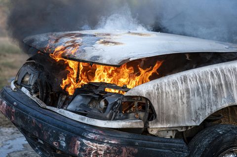 Primo piano del motore di automobile che brucia dopo una collisione di incidente frontale sul bordo della strada con fiamma e fumo. close up of burning car engine after a frontal crash collision on the roadside with flame and smoke