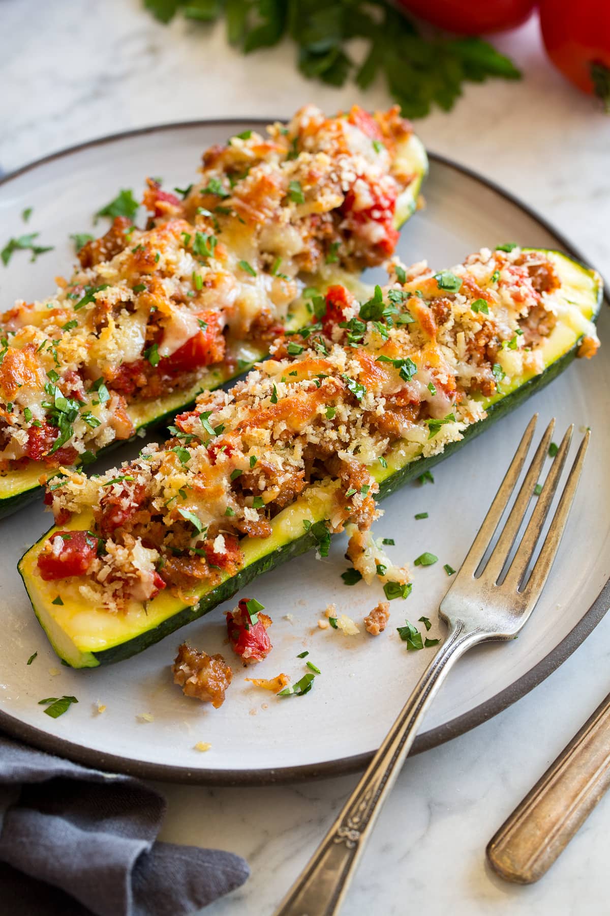 Zucchine a barchetta Two stuffed zucchini boats on a white dinner plate with a fork to the side.