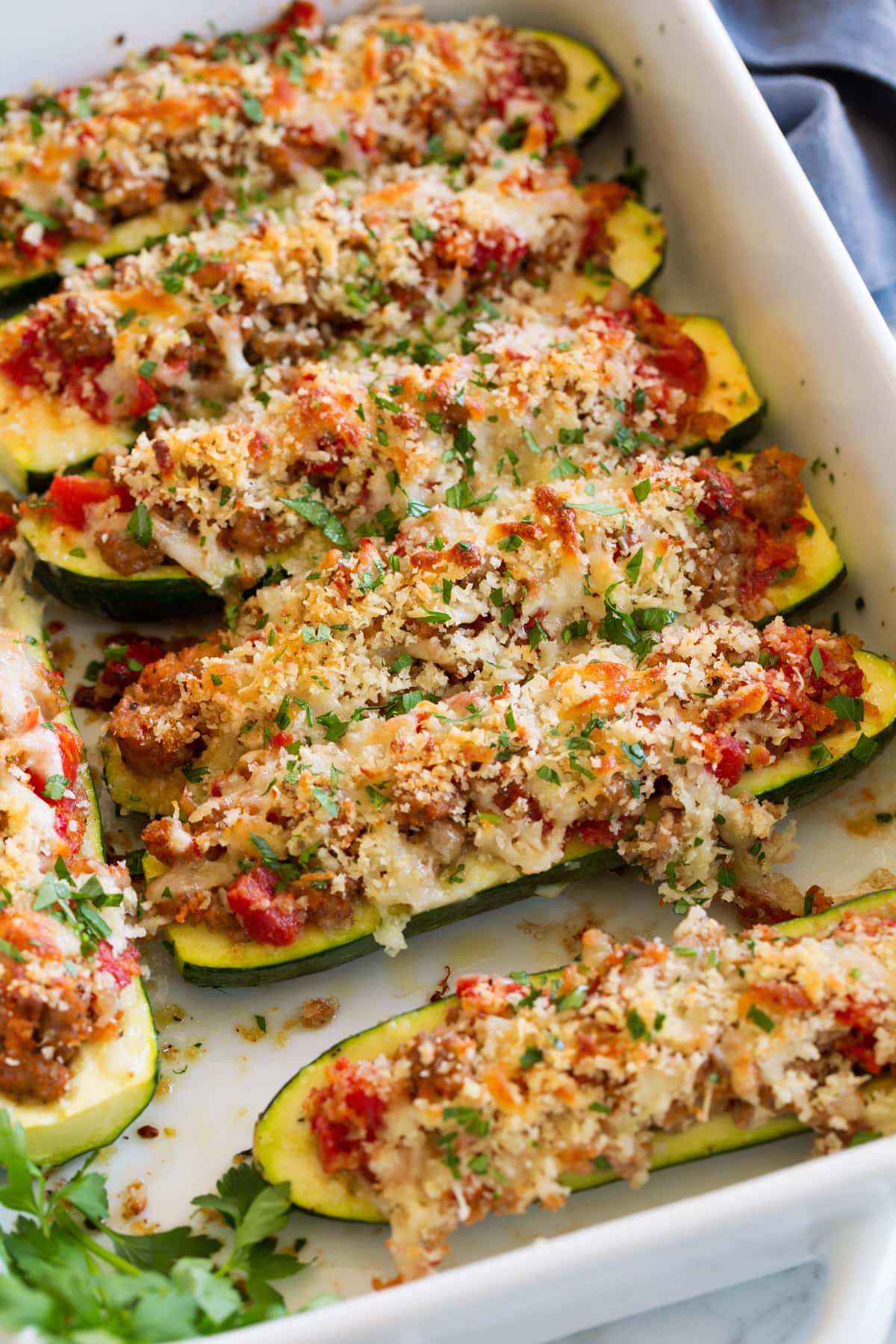 Zucchine Ripiene Di Salsiccia Image of zucchini boats stuffed with sausage, tomatoes, panko, and cheeses shown in a white baking dish.