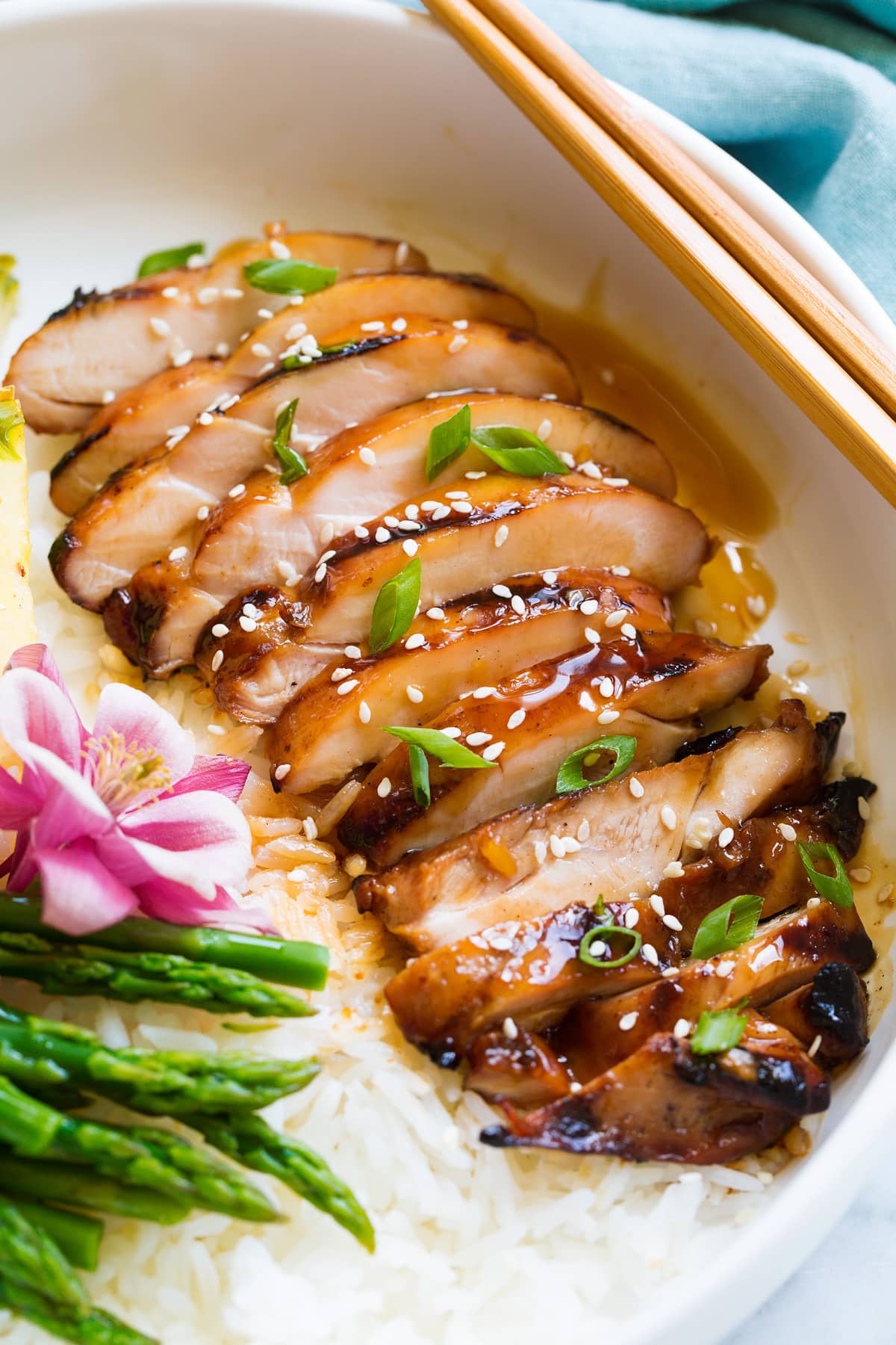 Pollo Teriyaki Alla Griglia Marinato Sliced chicken thigh shown after cooking, covered in teriyaki sauce, sesame seeds and green onions.
