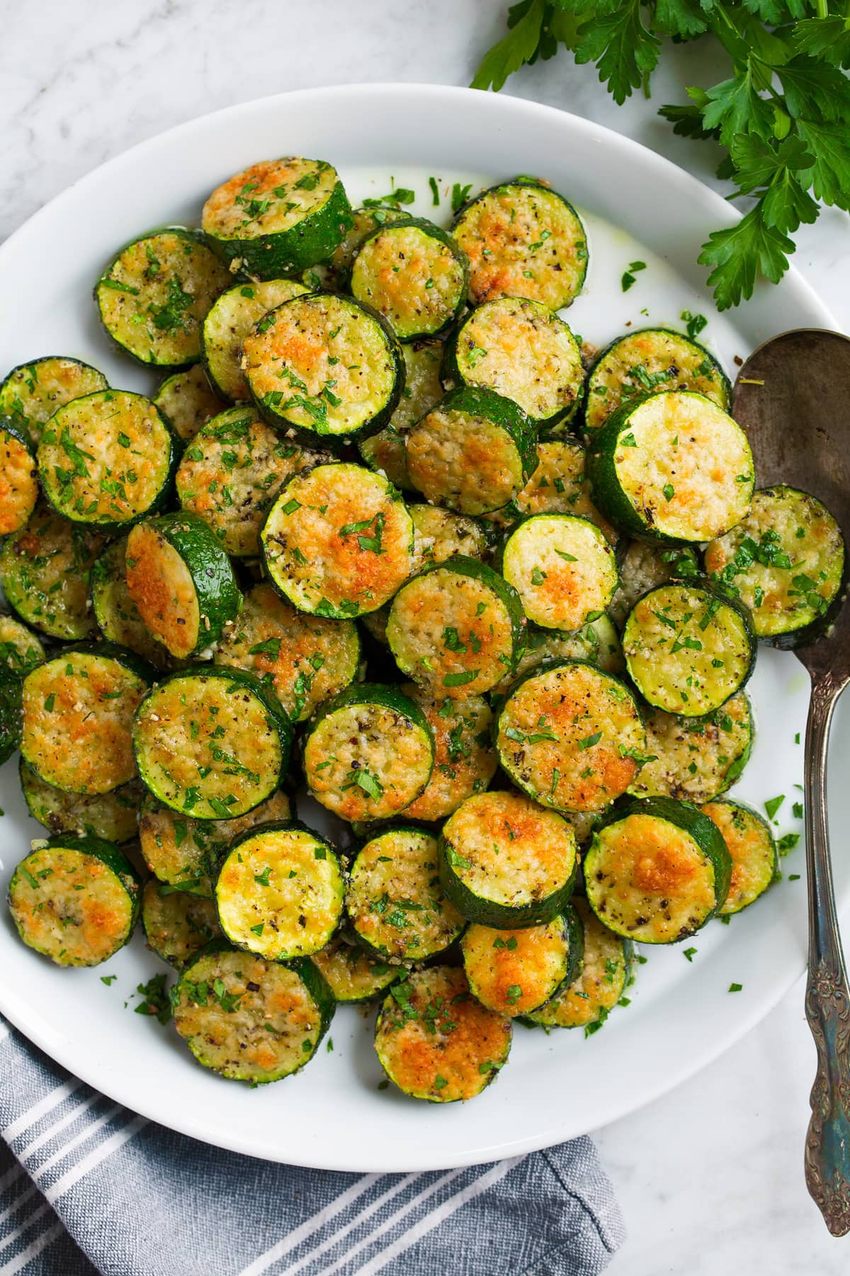 Zucchine Al Forno Baked zucchini coins covered with parmesan shown overhead on a white plate.