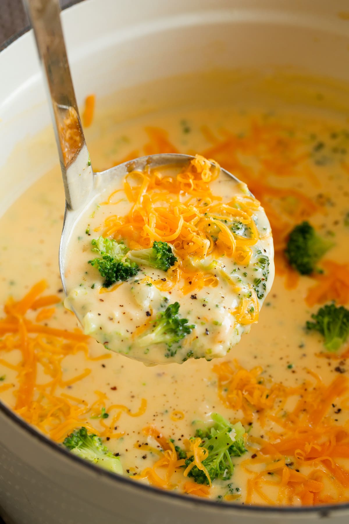 La MIGLIORE zuppa di formaggio e broccoli Ladle full of broccoli cheese soup lifted from a pot filled with soup.