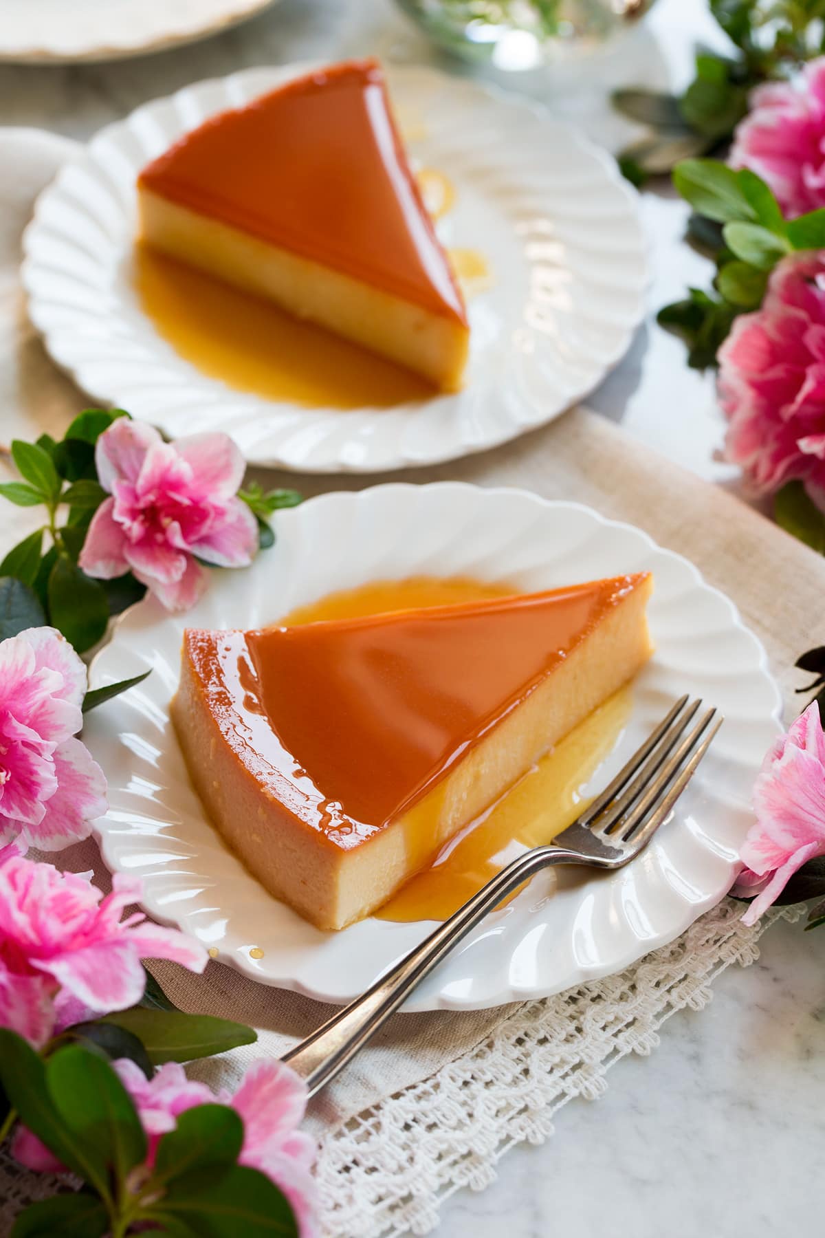 Ricetta Flan Image of two slices of flan on white scalloped plates with flowers around the sides.