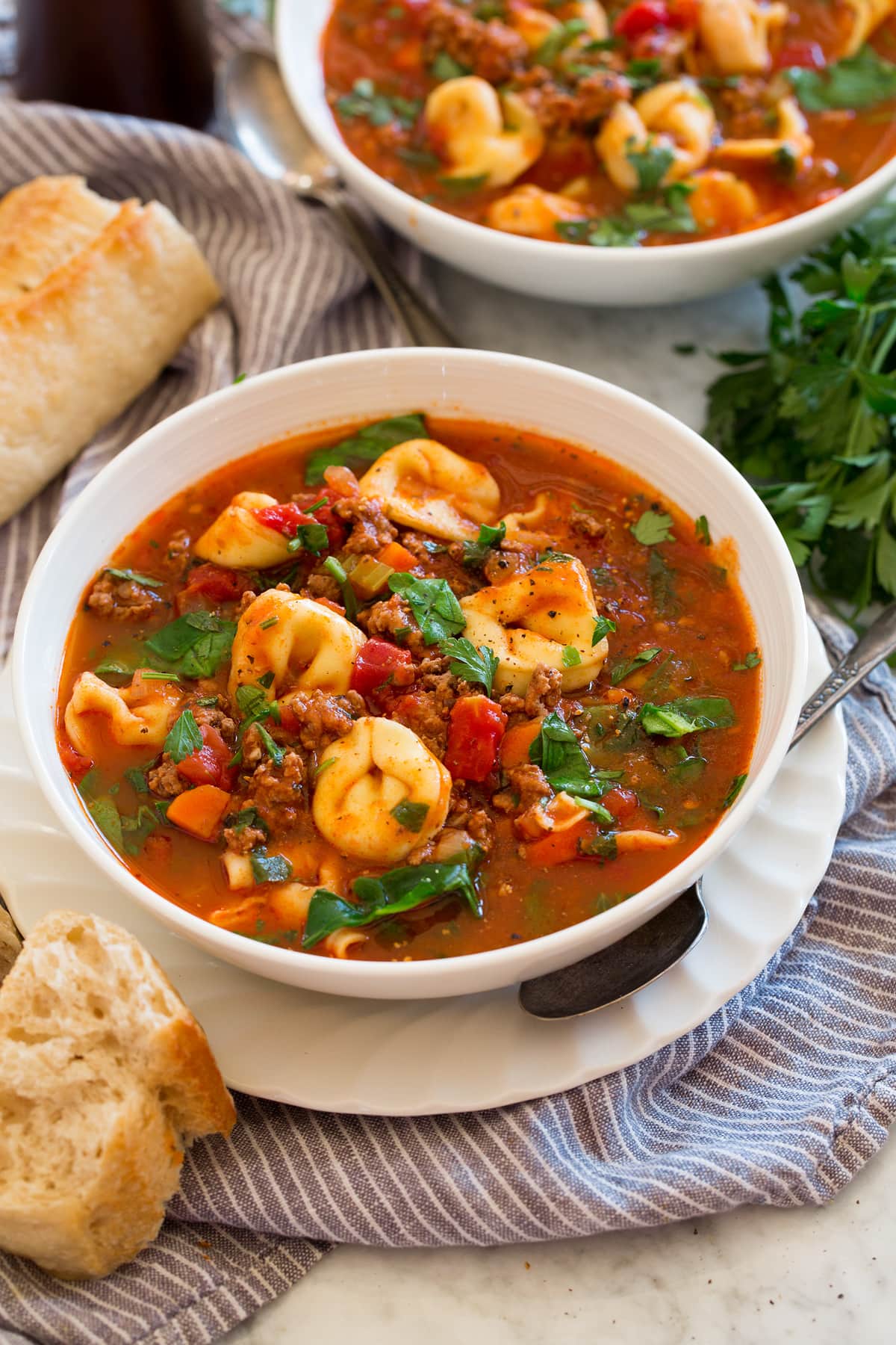 Two servings of tortellini soup in white bowls.